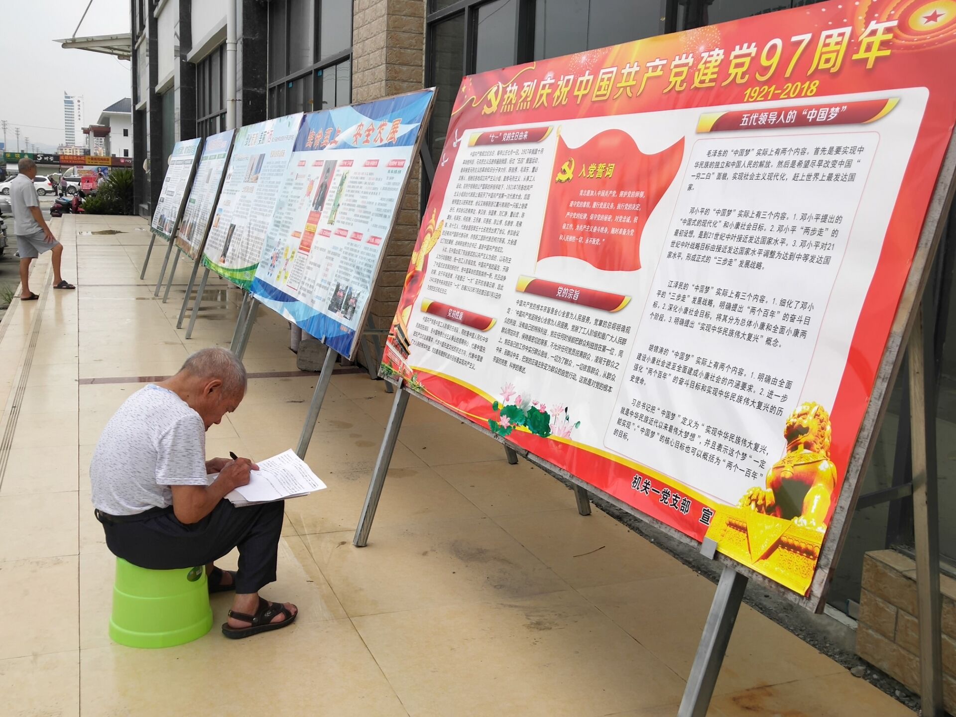 图为老党员在板报前抄写入党誓词